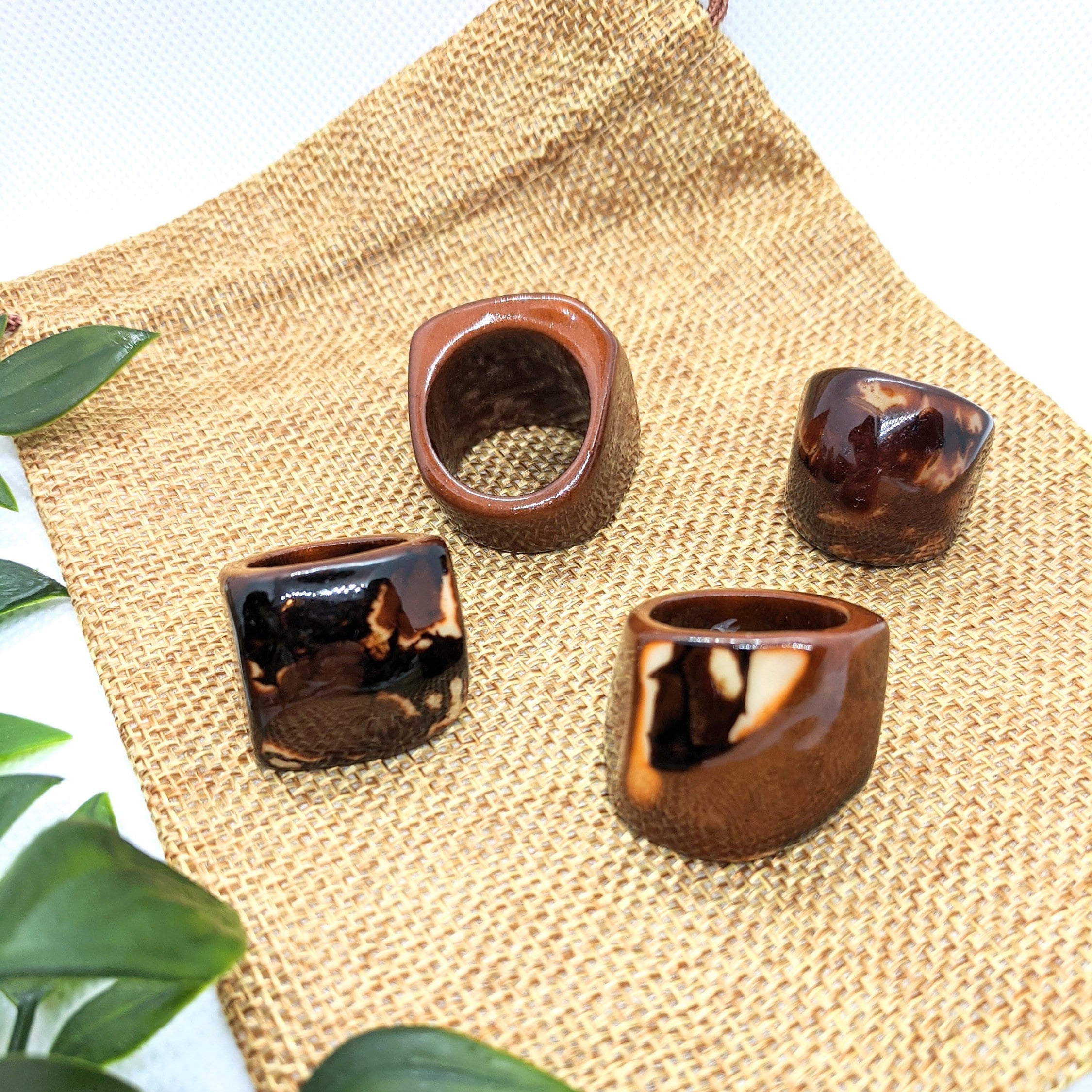 Set of four brown tagua nut rings on a woven mat with green leaves in the background