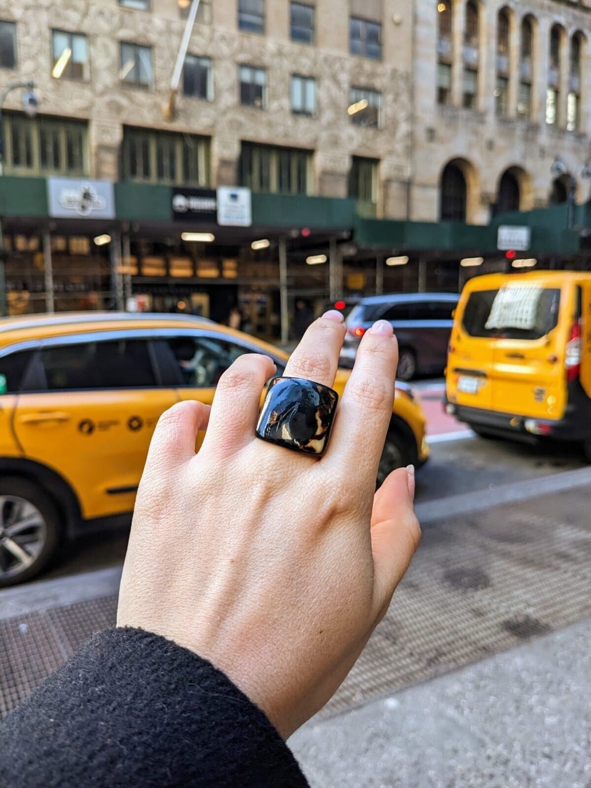 Hand wearing a black ring with a city street and yellow taxi in the background
