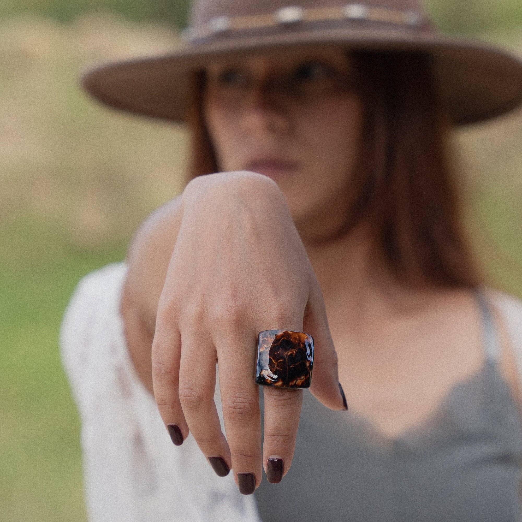 Person wearing a wide-brimmed hat and a ring with a distinctive design, standing in a natural setting.