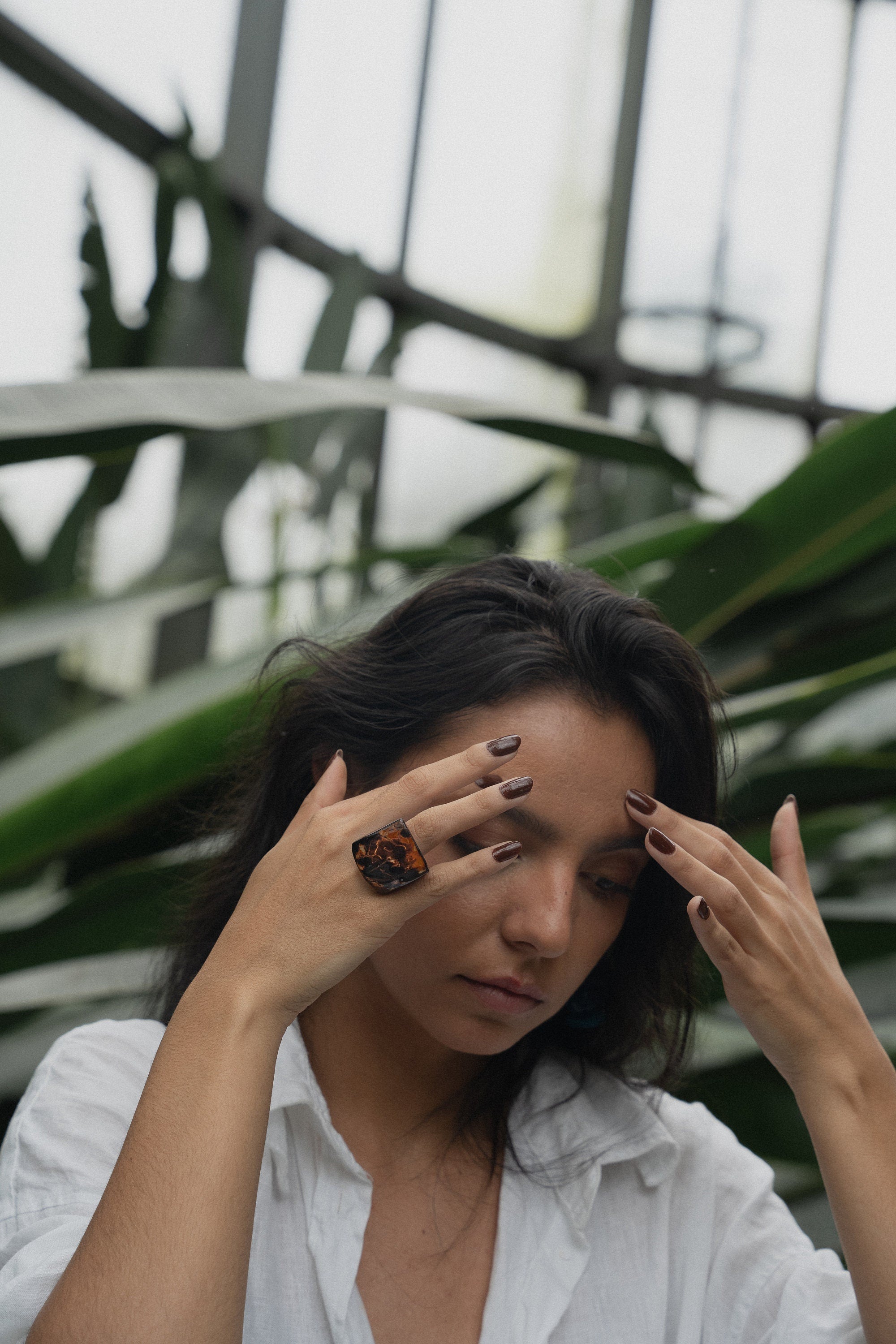 Woman with dark hair and white shirt and chunky ring in a greenhouse setting