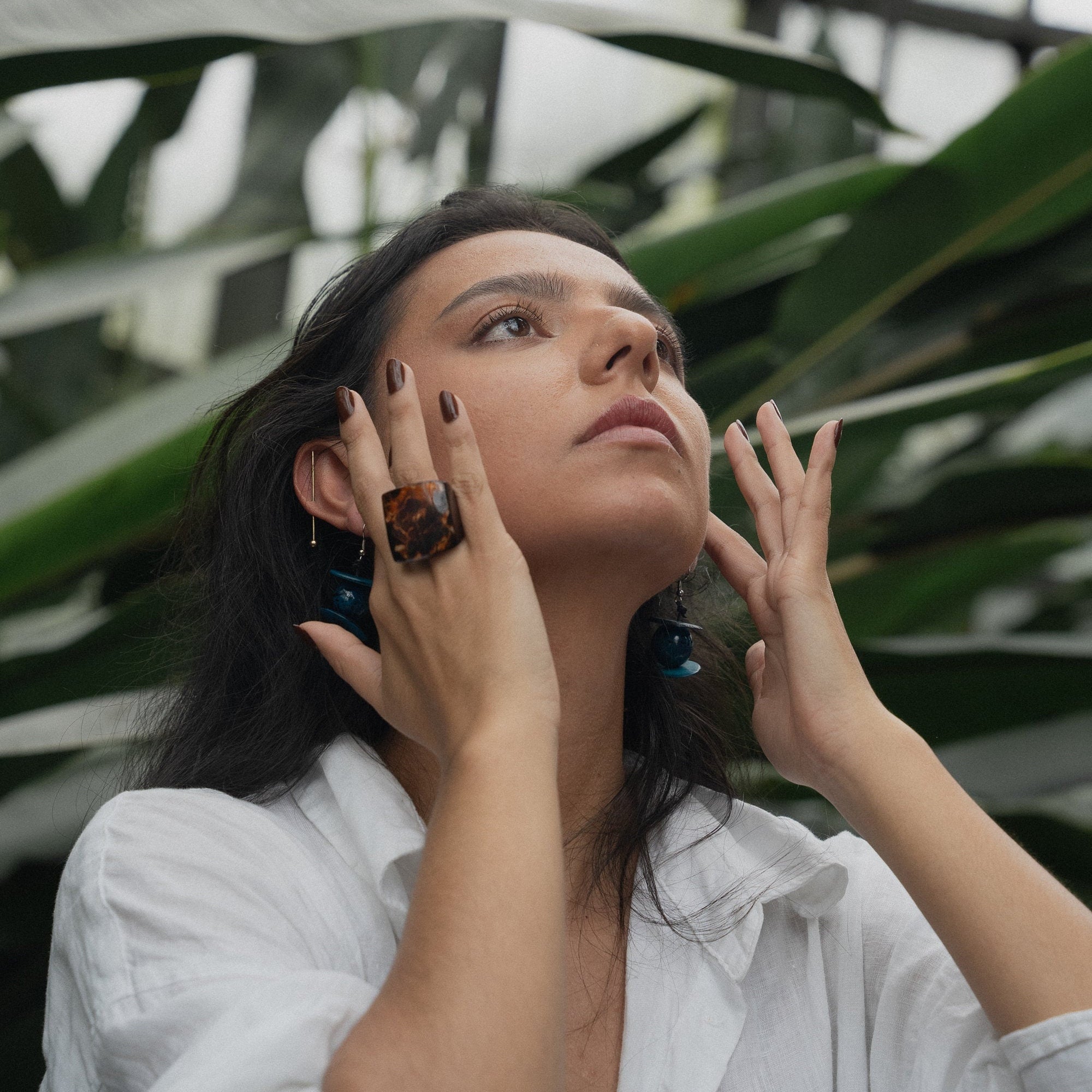 Woman wearing a chunky borwn ring with plants in the background