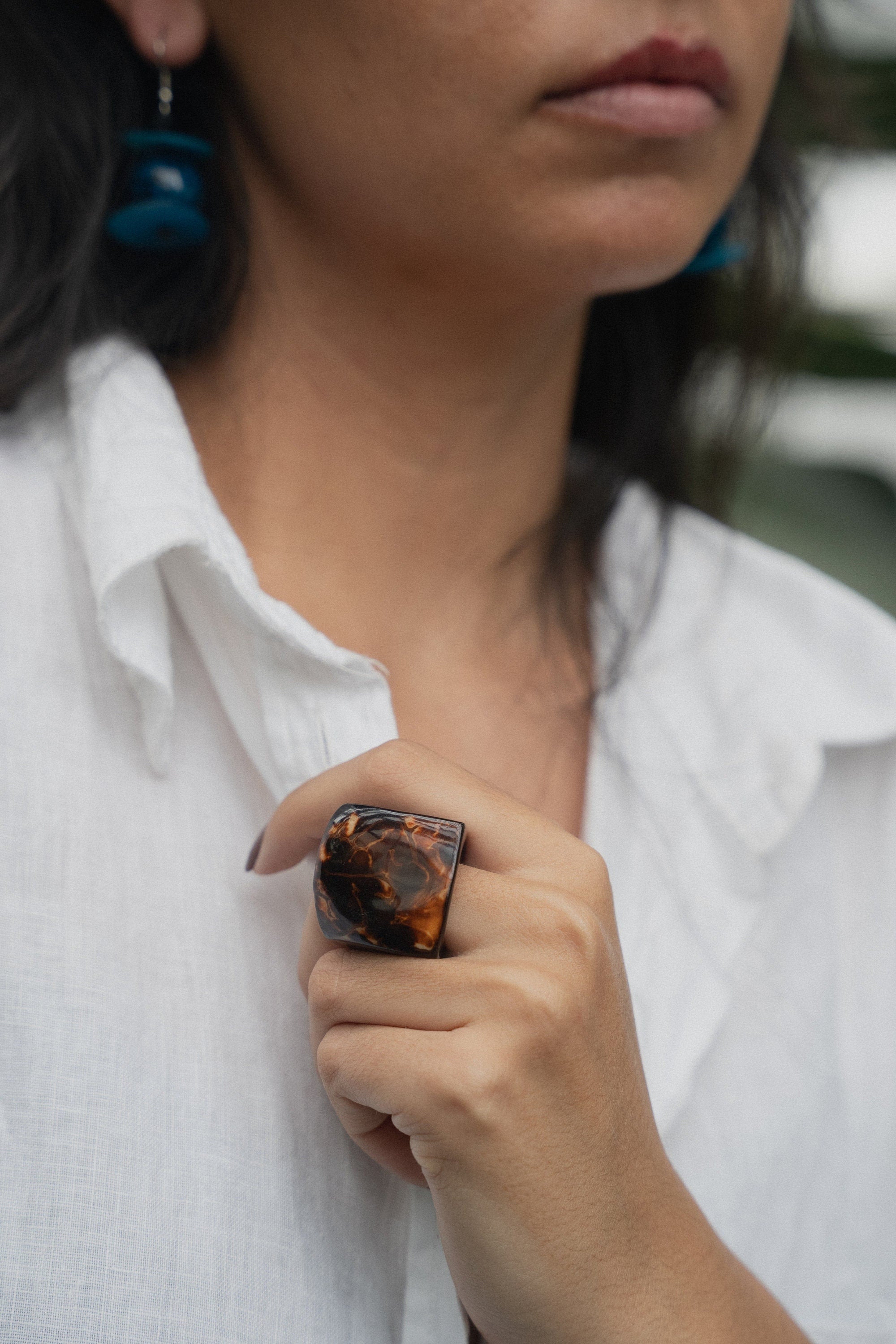 Person wearing a white shirt with a brown statement ring on a blurred background