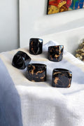 Set of six black rings on a white surface with a colorful abstract painting in the background.