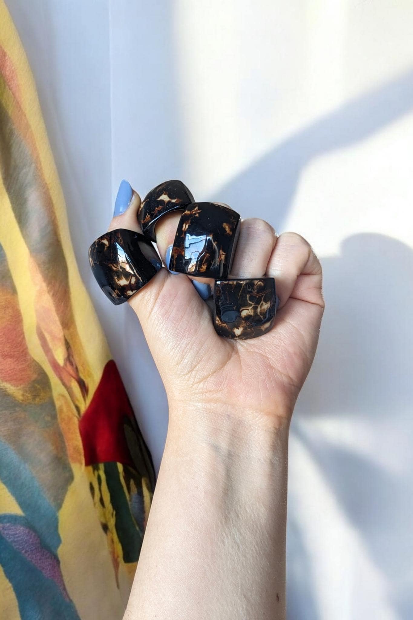 Hand holding handmade rings with a colorful scarf in the background