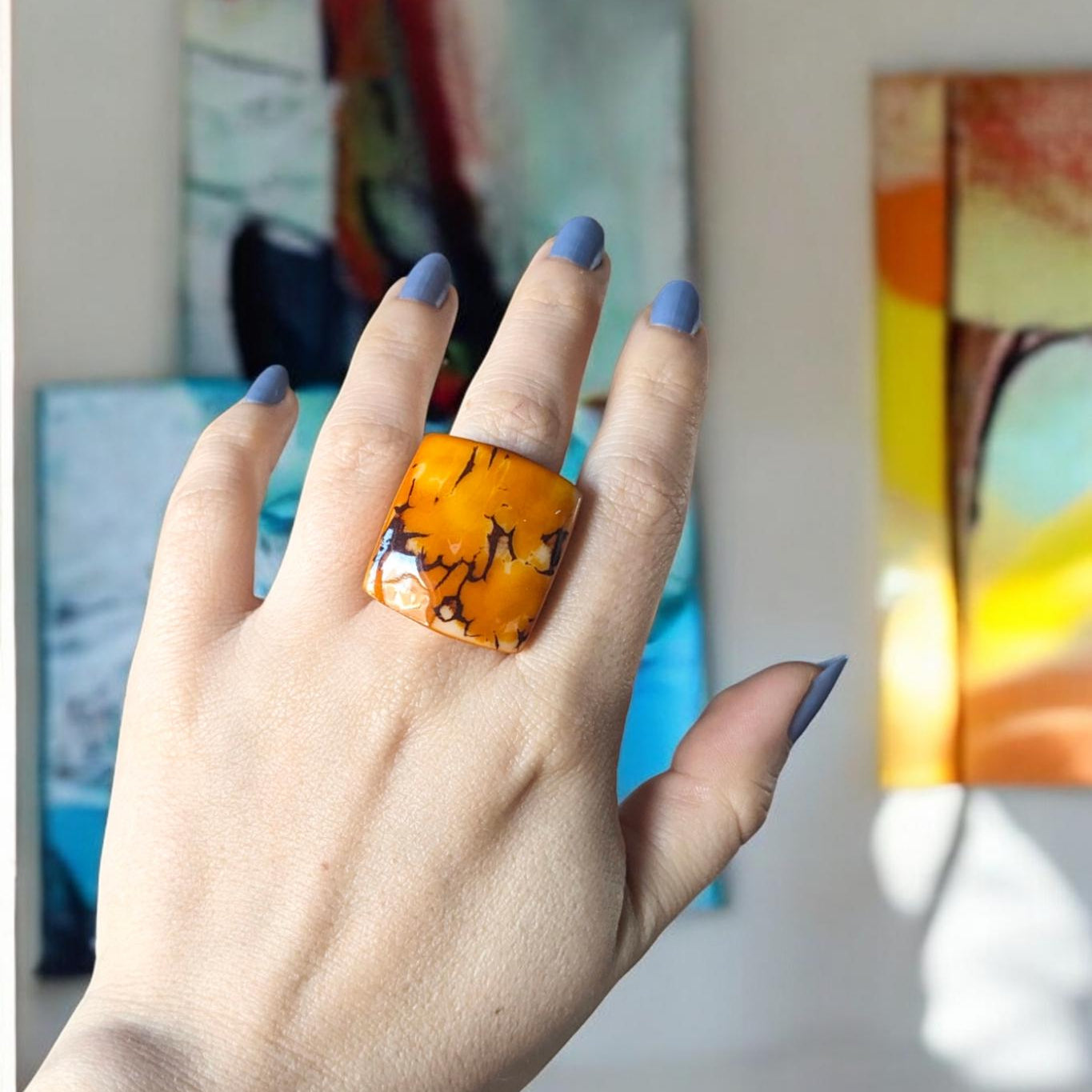 Hand wearing a beautiful ring with a colorful abstract painting in the background