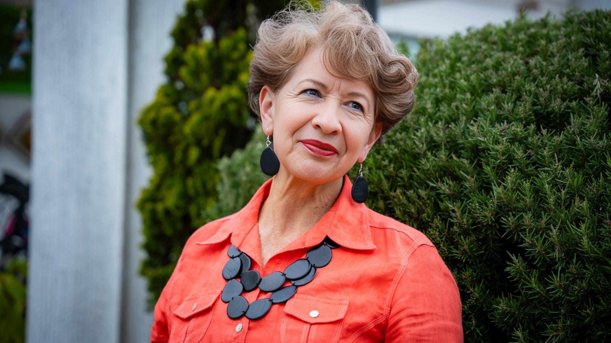 Woman wearing an orange shirt with a black necklace outdoors