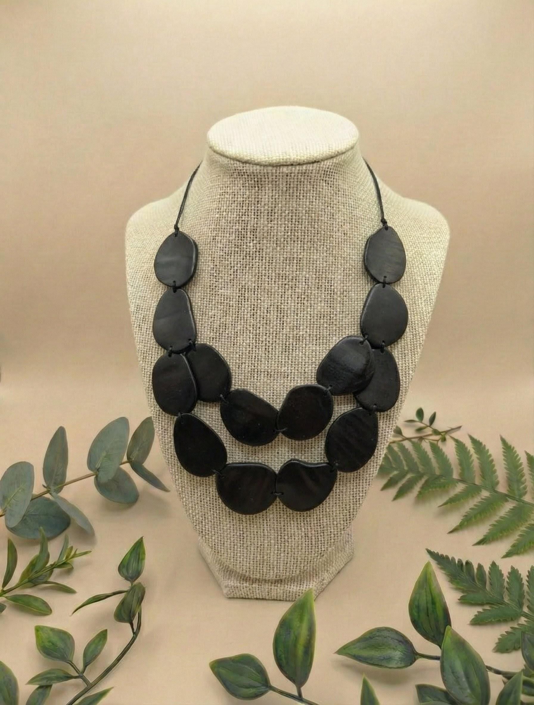 Black Tagua Nut necklace on a mannequin bust with green leaves in the background