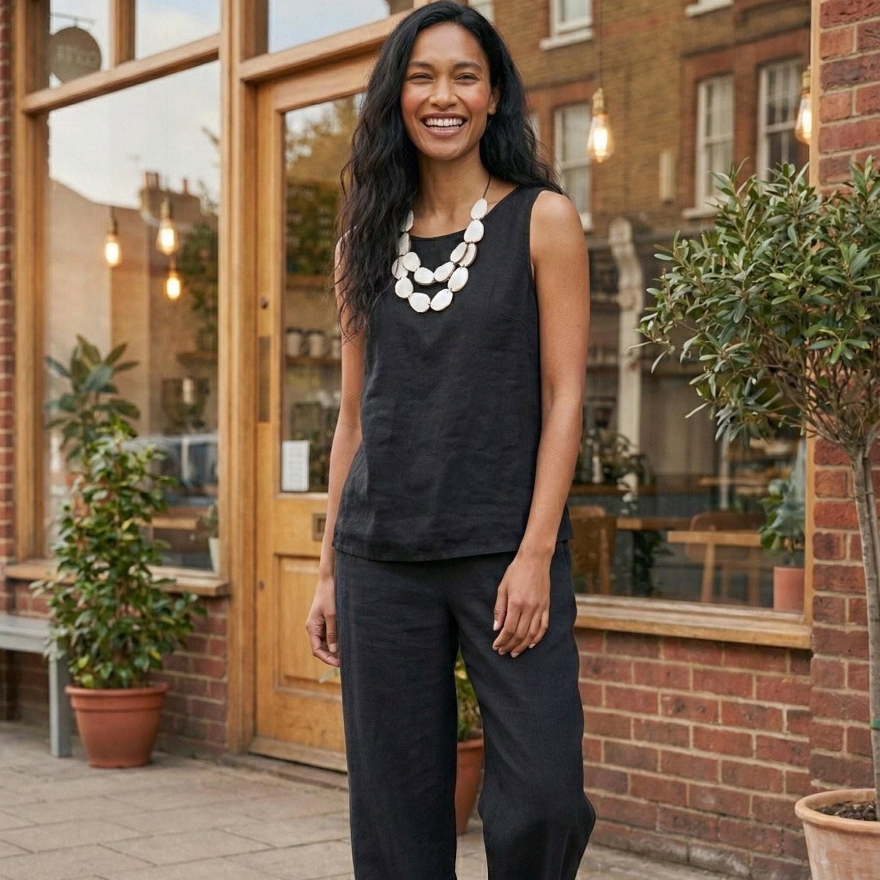 Woman in black sleeveless top and wide-leg pants standing outdoors near a brick building.